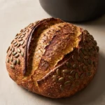 Kürbisbrot mit Sauerteig: Ganzer runder Brotlaib mit knuspriger Kruste, tiefem Ausbund und gerösteten Kürbiskernen.