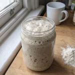 Aktiver Sauerteig im Glas, verdoppeltes Volumen mit vielen sichtbaren Bläschen und Wölbung.