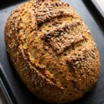 Saftiges Low Carb Brot mit Magerquark: Ovaler saatenreicher Laib mit zwei Einschnitten goldbraun auf dem Backblech.